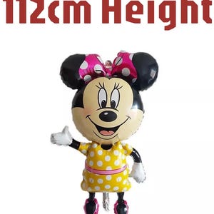 Może przedstawiać: Balon foliowy w kształcie Myszki Minnie, przedstawiający ż&oacute;łtą sukienkę w białe kropki, r&oacute;żową kokardę w białe kropki oraz białe rękawiczki. Balon posiada nadruk 112cm Height. Postać ma czarne uszy, beżową twarz i uśmiech.