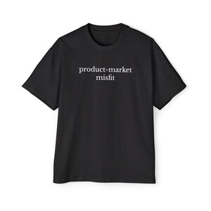 May include: A black short-sleeved t-shirt featuring the white text "product-market misfit" printed in a serif font across the center of the chest. The garment has a crew neckline and a standard fit with straight hemmed sleeves and bottom edge.