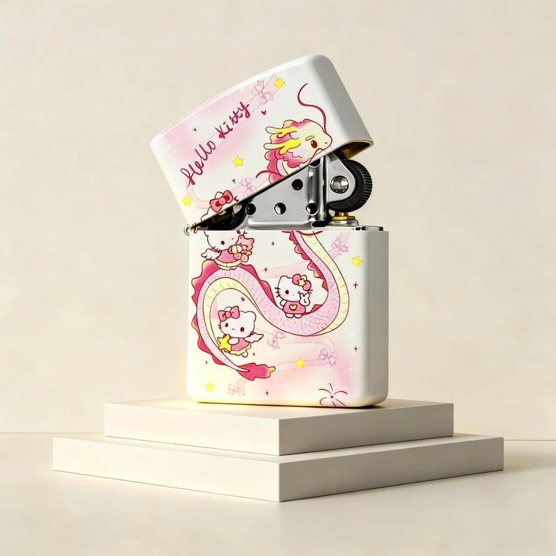 May include: A white metal flip-top lighter featuring a pink and yellow dragon graphic with Hello Kitty characters. The text Hello Kitty is printed in a cursive script on the lid. The lighter is open, revealing the internal metal mechanism.