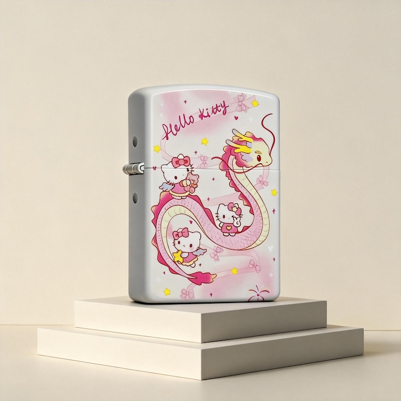 May include: A white metal flip-top lighter featuring a graphic of Hello Kitty characters and a long pink dragon. The design includes the text Hello Kitty in pink script, small yellow stars, and pink hearts against a soft pink background.