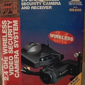 May include: A boxed 2.4 GHz wireless security camera system. The box features a black camera and receiver, with the text "2.4 GHz Wireless Security Camera and Receiver". The box also includes the text "Protect your home, office or small business investment."