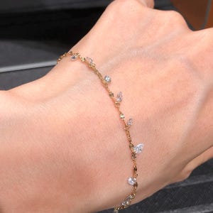 May include: A delicate gold chain bracelet featuring small, clear, faceted stones spaced along the length of the chain. The stones are set in a variety of shapes, including round and pear-like cuts, creating a subtle, shimmering effect on the wrist.