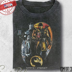 May include: A charcoal grey acid-wash t-shirt featuring a graphic print of Mortal Kombat characters Scorpion and Sub-Zero holding soda cans. The design includes a circular yellow background, the Mortal Kombat dragon logo, and the text Mortal Kombat.