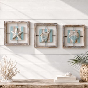 Peut inclure: Trois décorations murales carrées représentant une étoile de mer, un coquillage conque et une coquille Saint-Jacques. Chaque pièce est encadrée de bois brun vieilli sur un fond de planches verticales bleu clair et blanc.