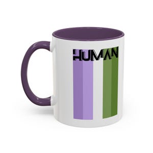 May include: A white ceramic mug with a purple handle and interior rim. The front features the word HUMAN in bold black capital letters positioned above two vertical rectangular stripes, one in light purple and one in olive green.