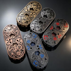 May include: Five oval-shaped metal fidget spinners featuring intricate gear and clockwork designs. The spinners are finished in various metallic tones including bronze, silver, and black, with some models showcasing red or blue accents behind the gears.