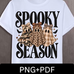 Op de afbeelding: Een wit t-shirt met de zwarte tekst SPOOKY SEASON en drie geesten met strikken. De geesten hebben camouflage-, luipaard- en bruin ruitpatronen. Kleine zwarte vleermuizen en bruine hartjes zijn verspreid rondom de geesten afgebeeld.