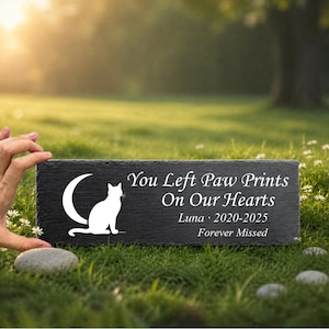 May include: A rectangular black slate memorial plaque featuring a white silhouette of a cat sitting in front of a crescent moon. The text reads: You Left Paw Prints On Our Hearts, Luna 2020-2025, Forever Missed, engraved in white lettering.