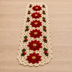 May include: A rectangular crochet table runner in cream yarn featuring a repeating pattern of six large red poinsettia flowers with yellow centres, accented by small green leaves and clusters of three red berries along the scalloped edges.