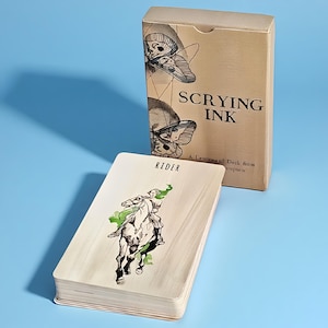 Könnte beinhalten: Ein Scrying Ink Lenormand-Kartendeck mit einer beigen Schachtel, die Mottenillustrationen und den Text Scrying Ink zeigt. Eine einzelne Karte liegt davor und zeigt eine schwarz-weiße Tuschezeichnung eines Reiters mit grünen Akzenten und dem Wort Rider am oberen Rand.