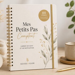 May include: A white spiral-bound notebook with gold wire binding and a gold elastic closure. The cover features the text Mes Petits Pas Comptent, Carnet de Suivi et de Motivation, Silver & Glow, and 60 Pages, with a botanical illustration.