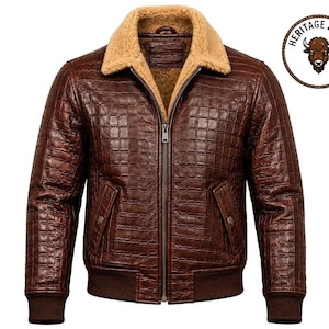 May include: A dark brown jacket with a textured grid pattern, a tan faux-fur collar, and a front zipper closure. The jacket features ribbed cuffs and hem, two side pockets with snap buttons, and a circular logo reading Heritage Hides.