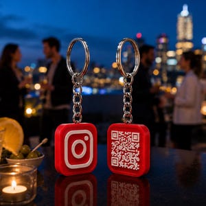 May include: Two square red keychains with silver metal rings and chains. One keychain features a white Instagram logo, while the other displays a white QR code. The keychains are positioned upright, showcasing their distinct front-facing designs.