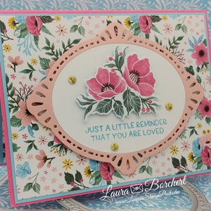Könnte beinhalten: Eine Karte mit rosa-weißem Blumenmuster, einem rosa ovalen Rahmen und einem weißen Oval im Inneren. Das weiße Oval zeigt ein Blumenmuster und den Text "JUST A LITTLE REMINDER THAT YOU ARE LOVED".