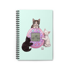 Peut inclure: Un carnet à spirales avec une couverture vert menthe clair illustrant un jouet animal virtuel. Un chaton calico est assis au-dessus, un chaton noir appuie sur un bouton et un chaton blanc lèche le côté de l'appareil rose orné d'étoiles.