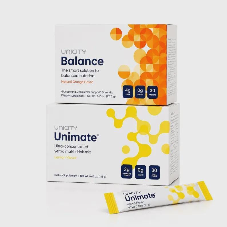 Puede incluir: Dos cajas rectangulares de suplementos diet&eacute;ticos Unicity apiladas verticalmente, con un sobre individual de Unimate delante. La caja superior es Balance con gr&aacute;ficos naranjas, la inferior es Unimate con gr&aacute;ficos y texto amarillos.