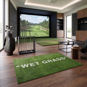 Peut inclure: Un tapis rectangulaire vert portant l'inscription "WET GRASS" en lettres capitales blanches. Le tapis est posé sur un parquet en bois sombre dans une pièce équipée d'un simulateur de golf, d'un sac de golf, d'un support de clubs et d'une table.