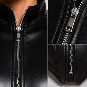 May include: A black faux leather garment featuring a high collar and a central silver-toned metal zipper. The design includes vertical seam detailing along the front, with a close-up view highlighting the metallic zipper teeth and pull tab.
