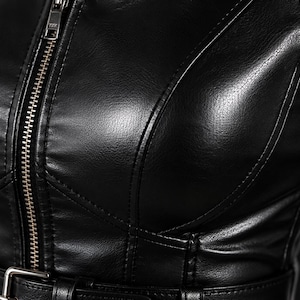 May include: A black jacket made of a smooth, leather-like material featuring a vertical silver-toned metal zipper closure running down the center. The garment includes structured seams across the chest and a matching black belt with a metal buckle.