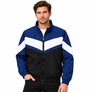 Puede incluir: Una chaqueta con cremallera que presenta un diseño de bloques de color con una sección superior azul, una franja blanca en forma de chevrón en el pecho y una sección inferior negra. La chaqueta incluye cuello alto, mangas largas con puños acanalados y dos bolsillos con cremallera.