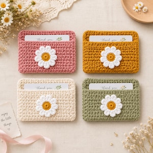 May include: Four rectangular crochet card holders in dusty pink, mustard yellow, cream, and sage green. Each holder features a white daisy appliqué with a yellow center and contains a white card printed with the text thank you.