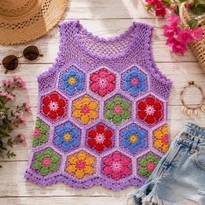 May include: A sleeveless crochet top featuring a lavender base with a hexagonal pattern of multi-colored floral motifs in red, blue, yellow, pink, and green. The garment has a scalloped hem and a delicate open-work mesh design at the neckline.