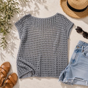 Flat lay of grey crochet mesh boxy tee with straw hat, sunglasses, denim shorts and sandals, summer crochet pattern