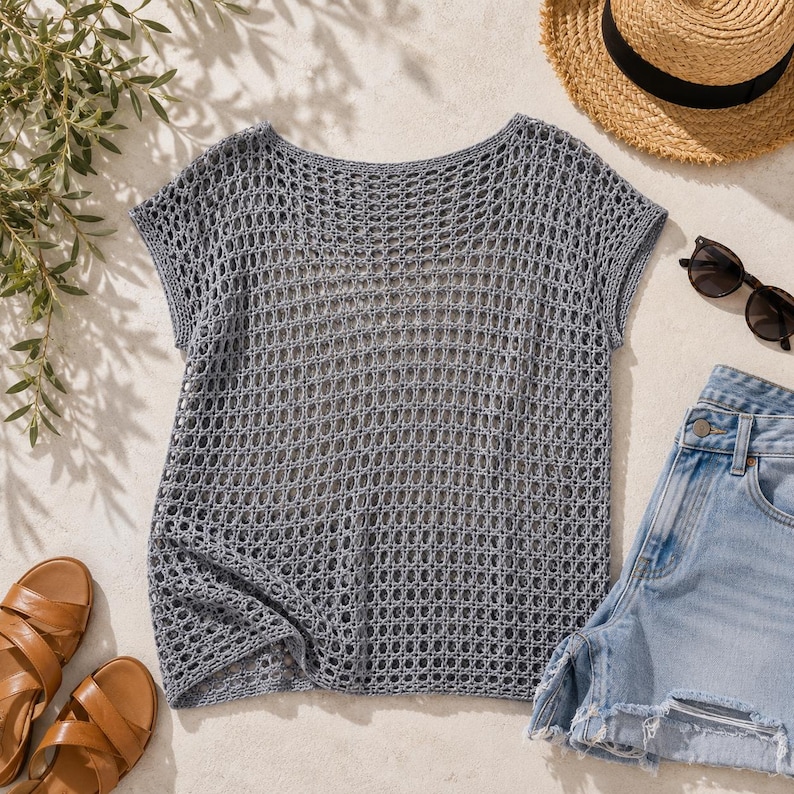 Flat lay of grey crochet mesh boxy tee with straw hat, sunglasses, denim shorts and sandals, summer crochet pattern