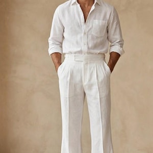 Op de afbeelding: Een wit overhemd met lange mouwen, knoopsluiting en borstzak, gecombineerd met een bijpassende witte broek met hoge taille, plooien aan de voorzijde en wijde pijpen. De outfit wordt gedragen met bruine leren loafers. De tekst 70sattire is zichtbaar.