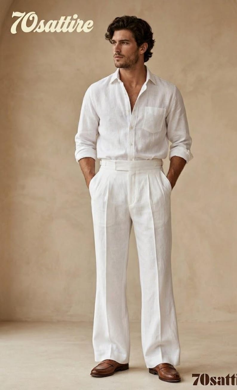 Op de afbeelding: Een wit overhemd met lange mouwen, knoopsluiting en borstzak, gecombineerd met een bijpassende witte broek met hoge taille, plooien aan de voorzijde en wijde pijpen. De outfit wordt gedragen met bruine leren loafers. De tekst 70sattire is zichtbaar.