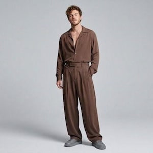 May include: A brown long-sleeve button-down shirt with a camp collar and matching brown pleated trousers with a belted waist. The outfit is paired with grey sneakers. The shirt is tucked into the trousers, creating a monochromatic brown ensemble.