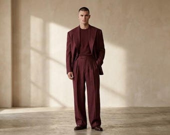 Könnte beinhalten: Ein tiefburgunderfarbener Anzug bestehend aus einem einreihigen Blazer mit breitem Revers, einem passenden Pullover mit Rundhalsausschnitt und einer Bundfaltenhose mit geradem Bein. Das Outfit wird durch dunkelbraune Leder-Loafer ergänzt.