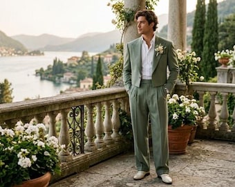 May include: A sage green suit consisting of a cropped blazer and high-waisted pleated trousers, worn with a crisp white button-down shirt. The blazer features a notched lapel adorned with a small white floral boutonniere, paired with light-colored shoes.