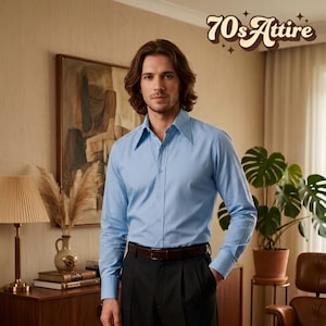 May include: A light blue long-sleeved button-down shirt with a wide pointed collar, worn tucked into black trousers with a dark brown leather belt. The text 70sAttire is visible in the upper right corner in a brown, rounded, retro-style font.