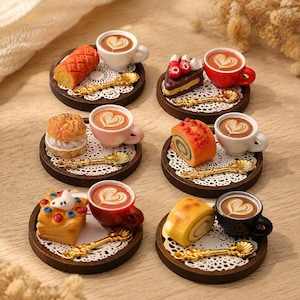 May include: Six miniature sets featuring small ceramic cups of coffee with heart-shaped latte art, assorted tiny pastries including cake slices and rolls, gold-toned decorative spoons, and white paper doilies on small circular wooden trays.