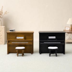 Pode incluir: Dois pianos verticais em miniatura, um com acabamento em madeira castanho-médio e outro com acabamento em preto sólido. Cada piano possui um teclado branco, uma estante com partitura impressa e um banco a condizer com assento branco.