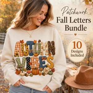 May include: A cream-colored sweatshirt featuring the text "AUTUMN VIBES" in large, patterned letters with various fall-themed prints, including plaid, sunflowers, and leopard spots, decorated with pumpkins, mushrooms, and leaves.