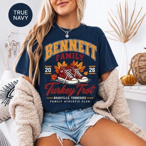 May include: A true navy short-sleeve t-shirt featuring a graphic with the text Bennett Family Turkey Trot, Nashville, Tennessee, Family Athletic Club, 2026. The design includes a pair of red sneakers surrounded by orange and yellow autumn leaves.