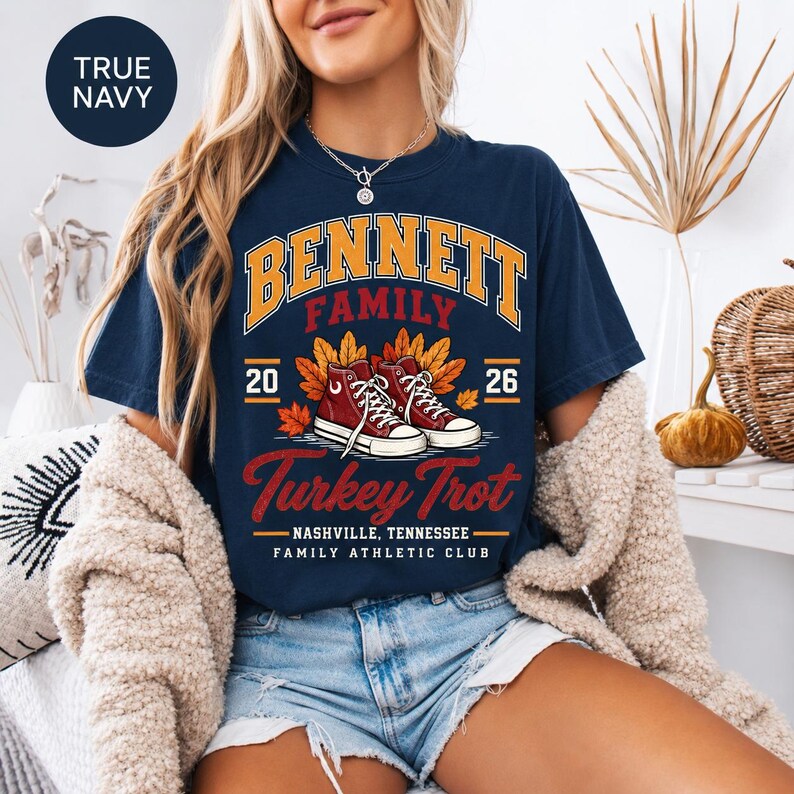 May include: A true navy short-sleeve t-shirt featuring a graphic with the text Bennett Family Turkey Trot, Nashville, Tennessee, Family Athletic Club, 2026. The design includes a pair of red sneakers surrounded by orange and yellow autumn leaves.