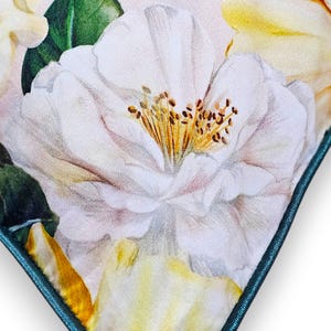 Peut inclure: Un coussin carr&eacute; arborant un imprim&eacute; botanique d&eacute;taill&eacute; de grandes fleurs de cam&eacute;lia blanches aux centres jaunes et aux feuilles vertes. Le coussin est fini avec un passepoil bleu sarcelle fonc&eacute; qui encadre le motif floral sur un fond clair.