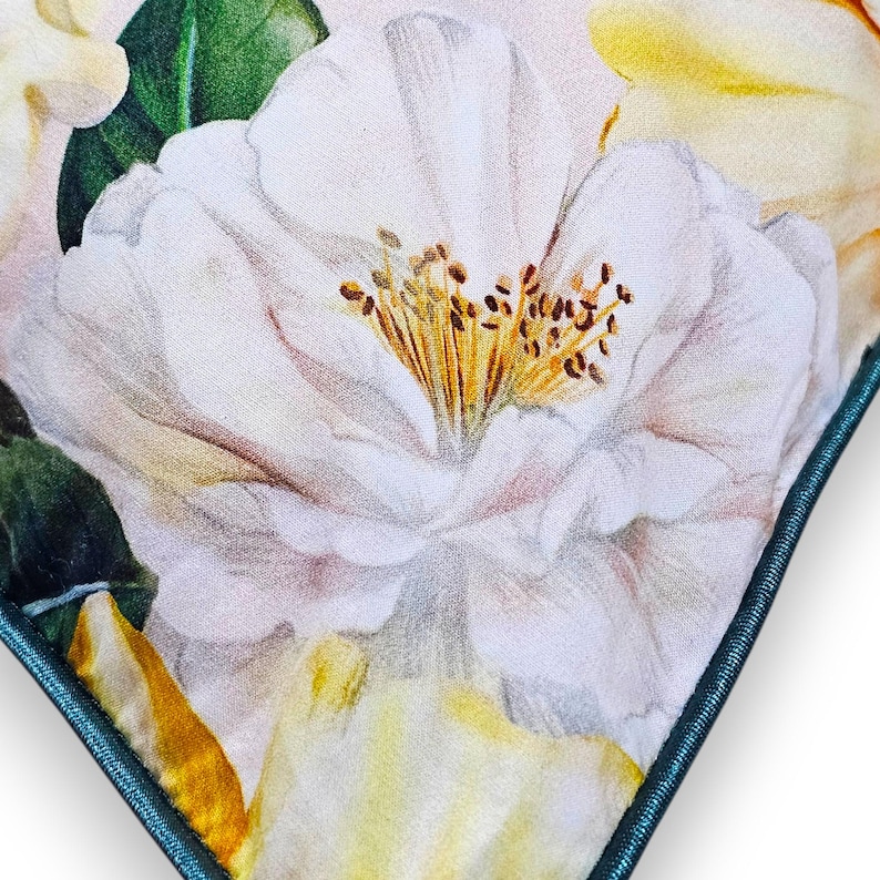 Peut inclure: Un coussin carr&eacute; arborant un imprim&eacute; botanique d&eacute;taill&eacute; de grandes fleurs de cam&eacute;lia blanches aux centres jaunes et aux feuilles vertes. Le coussin est fini avec un passepoil bleu sarcelle fonc&eacute; qui encadre le motif floral sur un fond clair.