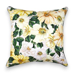Peut inclure: Un coussin carr&eacute; arborant un imprim&eacute; botanique compos&eacute; de grandes fleurs jaune p&acirc;le et blanches accompagn&eacute;es de feuilles vert fonc&eacute; sur un fond clair. Le tissu pr&eacute;sente le logo Dolce & Gabbana en petites lettres discr&egrave;tes parmi les motifs floraux.