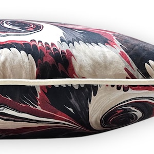 Puede incluir: Un coj&iacute;n rectangular con un patr&oacute;n jaspeado en tonos negro, rojo oscuro y crema. El coj&iacute;n tiene una superficie de tela suave al tacto y est&aacute; rematado con un ribete de tela de color crema a lo largo de la costura horizontal central.