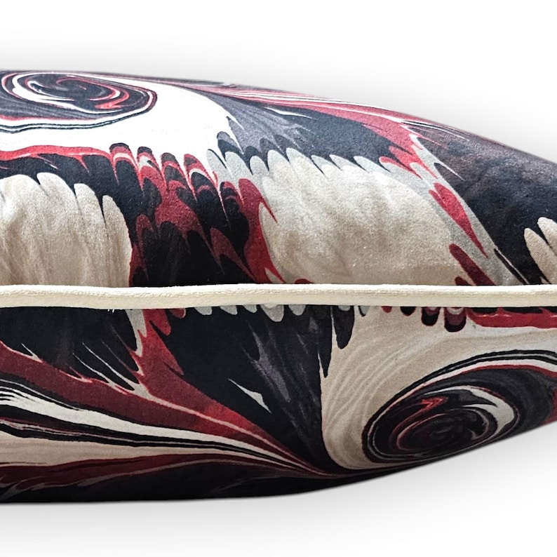 Puede incluir: Un coj&iacute;n rectangular con un patr&oacute;n jaspeado en tonos negro, rojo oscuro y crema. El coj&iacute;n tiene una superficie de tela suave al tacto y est&aacute; rematado con un ribete de tela de color crema a lo largo de la costura horizontal central.
