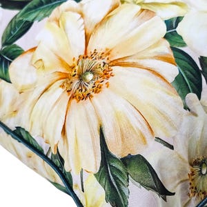 Peut inclure: Un coussin d&eacute;coratif pr&eacute;sentant un imprim&eacute; botanique &agrave; grande &eacute;chelle de fleurs jaune p&acirc;le avec des centres orange pro&eacute;minents et des feuilles vert fonc&eacute;. Le tissu a une texture lisse et est fini avec un passepoil vert fonc&eacute;.