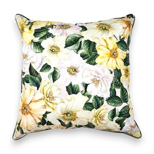 Peut inclure: Un coussin carr&eacute; orn&eacute; d'un imprim&eacute; botanique de fleurs jaunes et blanches avec des feuilles vert fonc&eacute; sur un fond clair. Le coussin pr&eacute;sente un passepoil vert fonc&eacute; et un logo manuscrit signature imprim&eacute; sur le tissu parmi le motif floral.