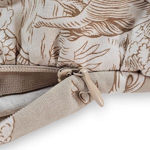 Puede incluir: Una funda de coj&iacute;n de tela beige con un patr&oacute;n toile de jouy marr&oacute;n de escenas pastorales. La funda incluye una cremallera oculta con un tirador beige a juego, integrado perfectamente en la costura del material textil texturizado.