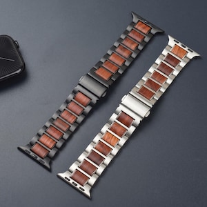 May include: Two watch bands featuring a link design with alternating metal and wood segments. One band is matte black metal with brown wood inlays, and the other is silver-toned metal with brown wood inlays. Both include a secure metal clasp.
