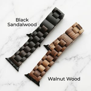 Puede incluir: Dos correas de reloj con diseño de eslabones. Una correa es de madera de sándalo negra y la otra de madera de nogal marrón. Ambas correas cuentan con conectores de metal negro en los extremos. El texto Black Sandalwood y Walnut Wood es visible.