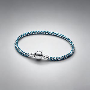 May include: A braided bracelet featuring a vibrant teal cord interwoven with polished silver-tone metal links. The bracelet includes a spherical silver-tone clasp engraved with the word PANDORA, connecting the two ends of the braided cord design.